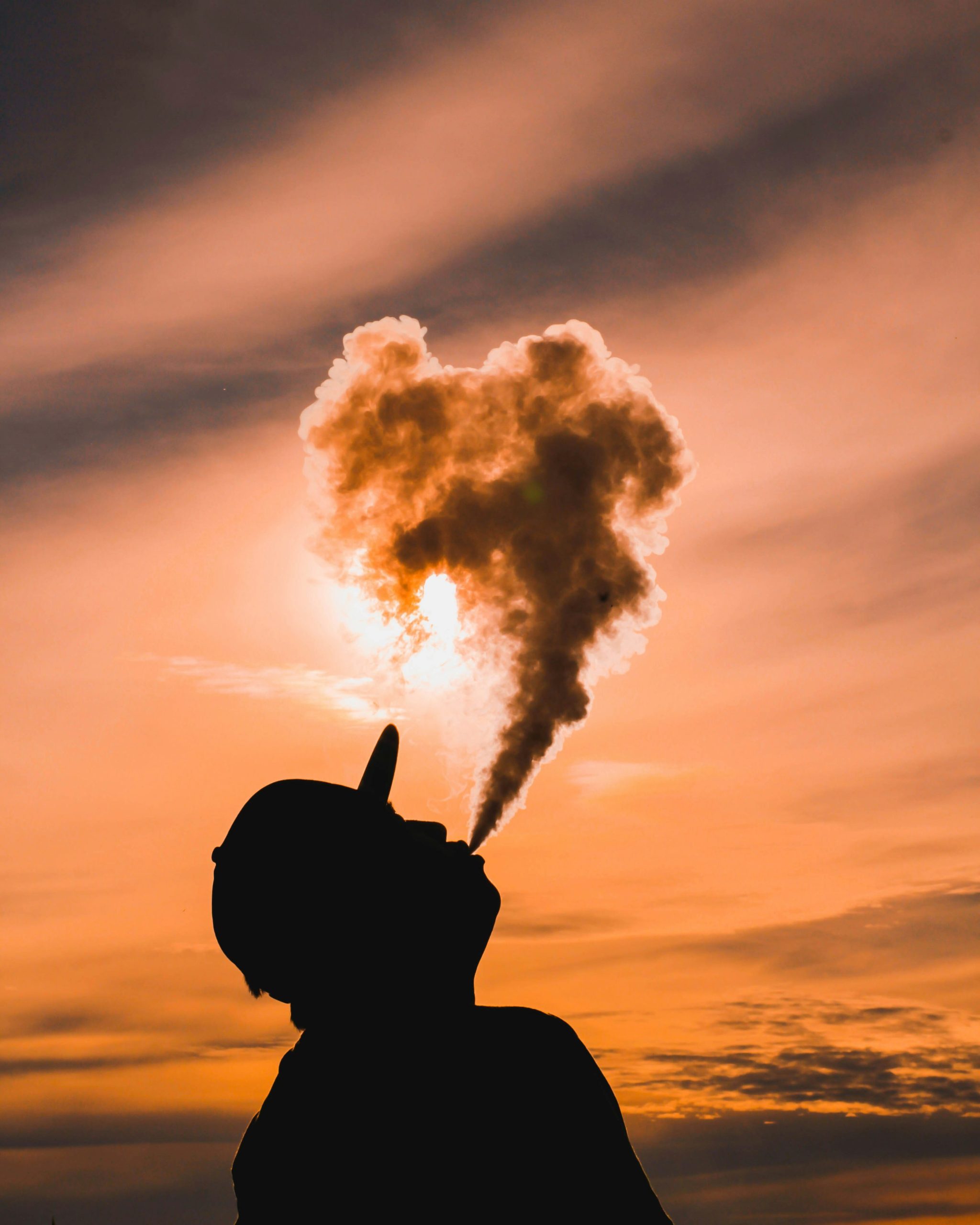 Teenager blowing smoke in the air against sunlight.